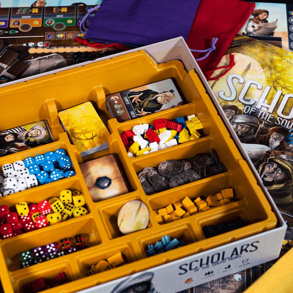 Board game components including dice and pieces in a yellow box with 'Scholars' branding.